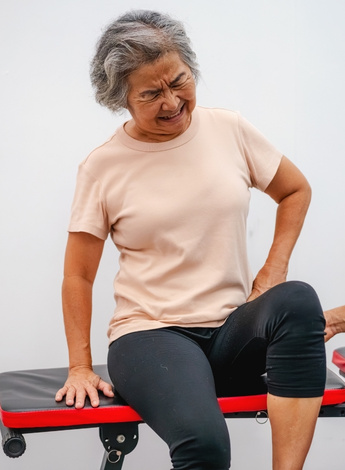 A woman sitting on a medical bed, clutching her hip in pain